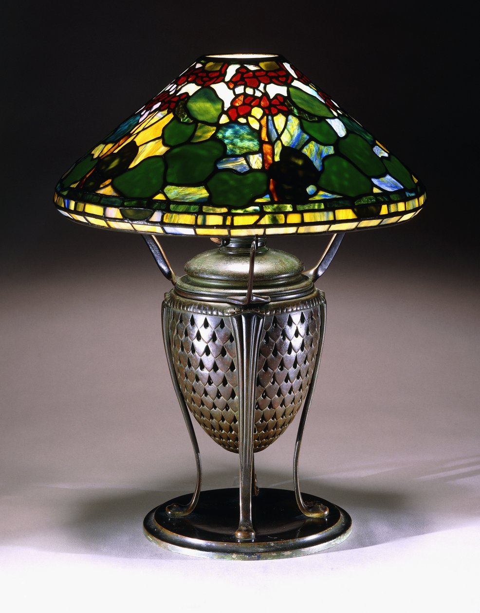 Een "Geranium" tafellamp met een conische kap, en geperforeerde bronzen urnvoet met een visschubbenpatroon, 20e eeuw door American School