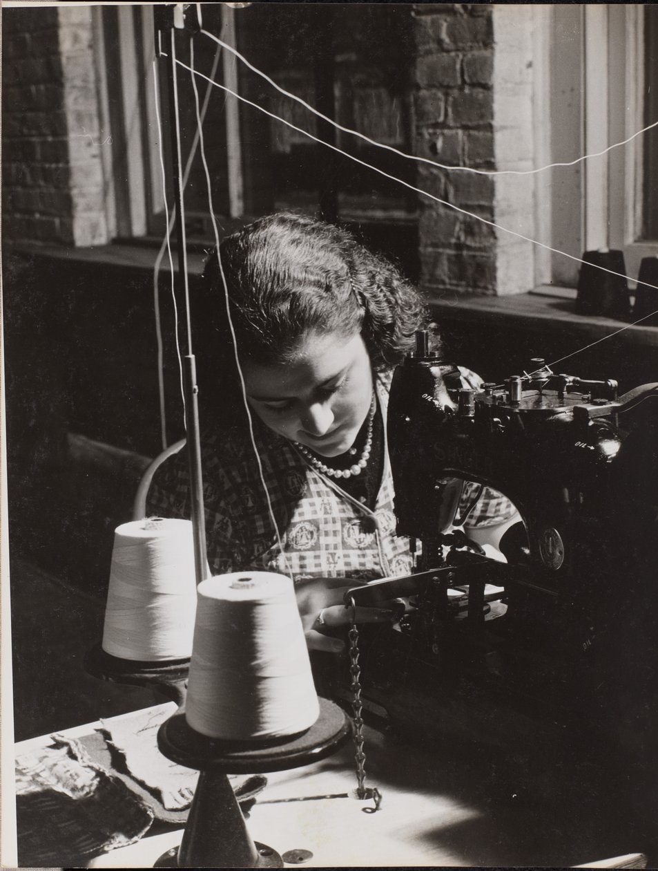 [Vrouw gebruikt een naaimachine met twee spoelen wit garen]. door Arnold Eagle