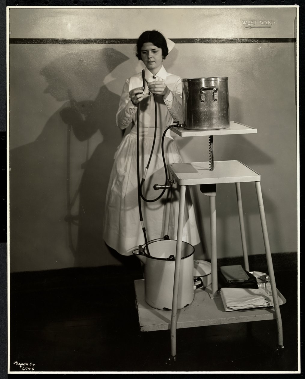 Een verpleegster demonstreert een speciaal apparaat met buizen en emmers voor aanvoer en afval in het Sloan Maternity Hospital, Broadway en 168th Street, New York, 1932 door Byron Company