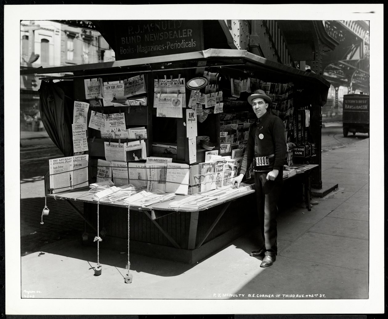 Blinde krantenverkoper P.J. McNulty bij zijn stand op de noordoostelijke hoek van 3rd Avenue en 42nd Street, New York, 1926 door Byron Company