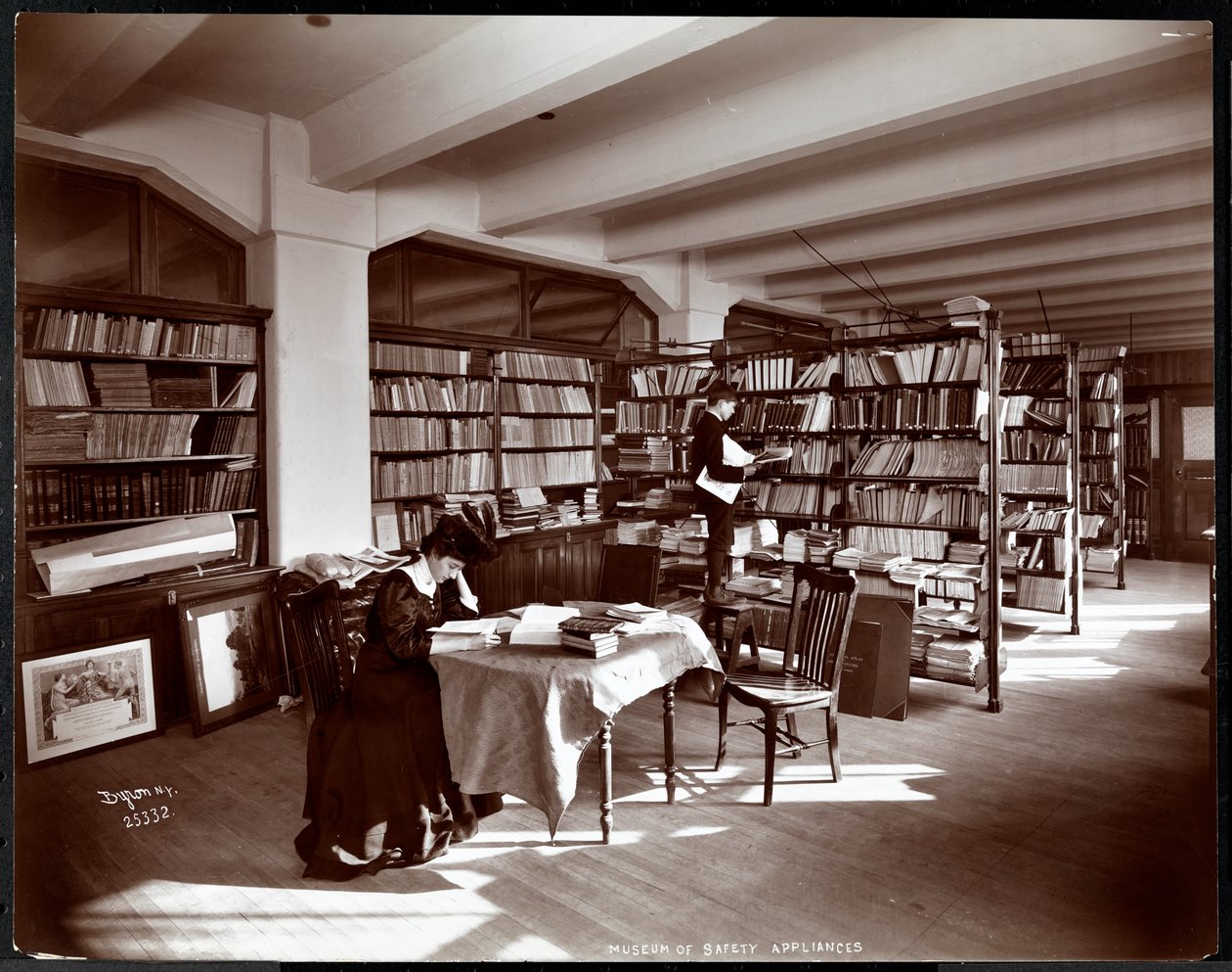 Vrouw en een jonge man in een bibliotheek van het Museum van Veiligheidsapparaten van het American Institute of Social Service, New York, 1907 (zilveren gelatin afdruk) door Byron Company