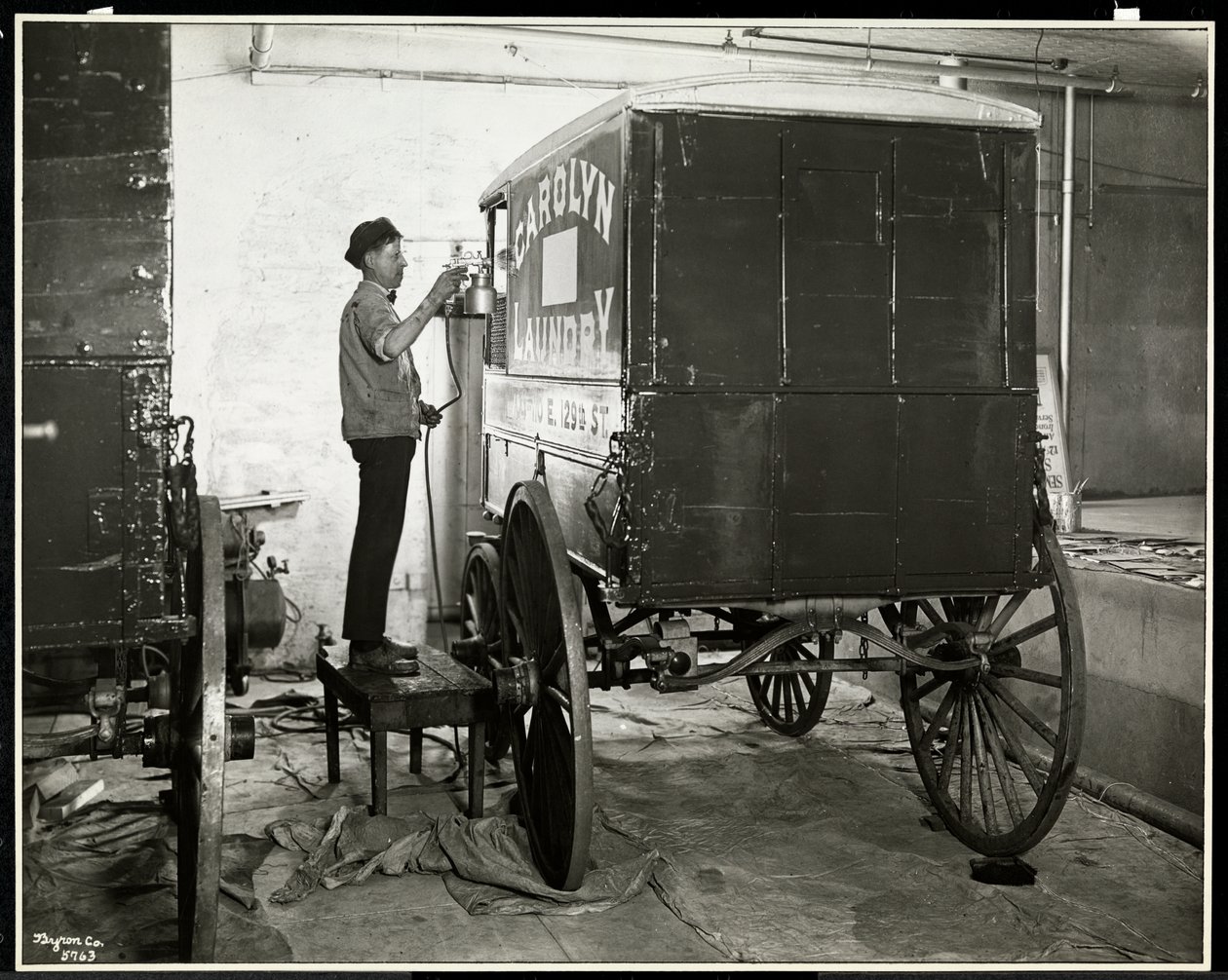 Een man die een bezorgwagen van de Carolyn Laundry spuitverft op 111 East 128th Street, East Harlem, New York, 1929 door Byron Company