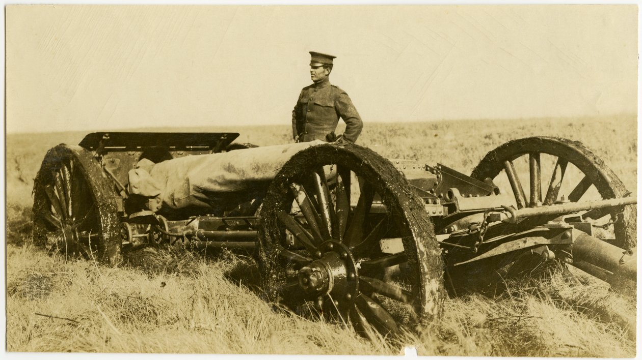 Horizontale sepiafoto van een man in uniform naast een artilleriekanon op wielen in een open veld door Carl Michel