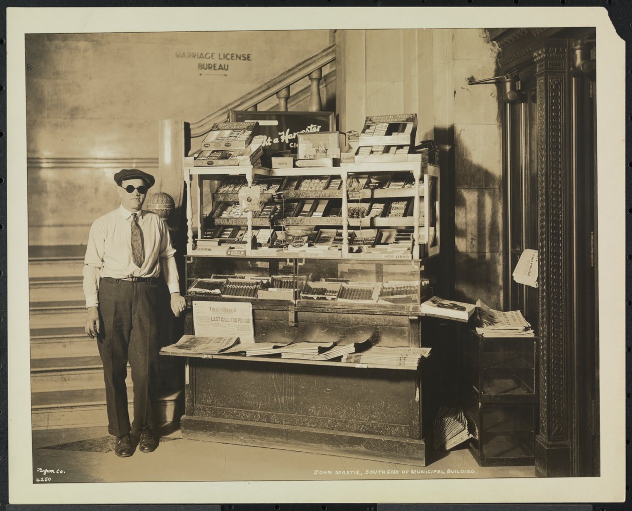 Blinde krantenverkoper, John Martie, bij zijn stand aan het zuideinde van het gemeentelijk gebouw, New York door Company Byron