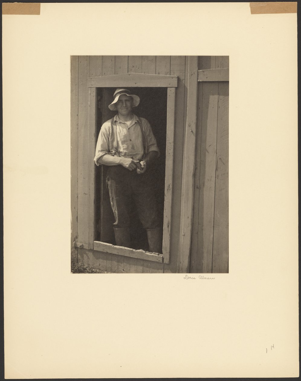 [Man met strohoed staat in de deuropening van een schuur en houdt een tabaksbuidel vast]. door Doris Ulmann