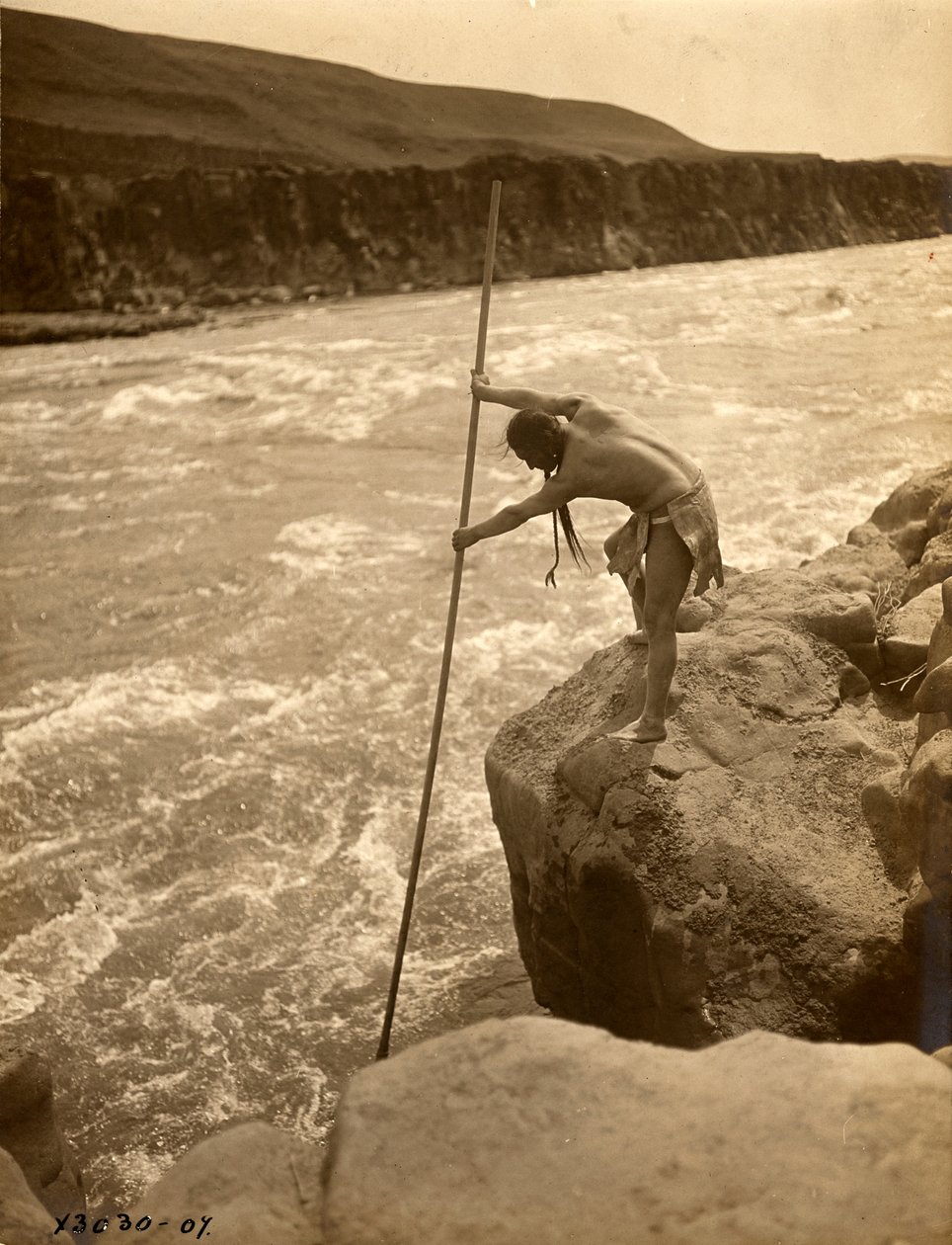 Tlakluit Indiaan, staand op rots, vist met schepnet, ca. 1910 (z/w foto) door Edward Sheriff Curtis