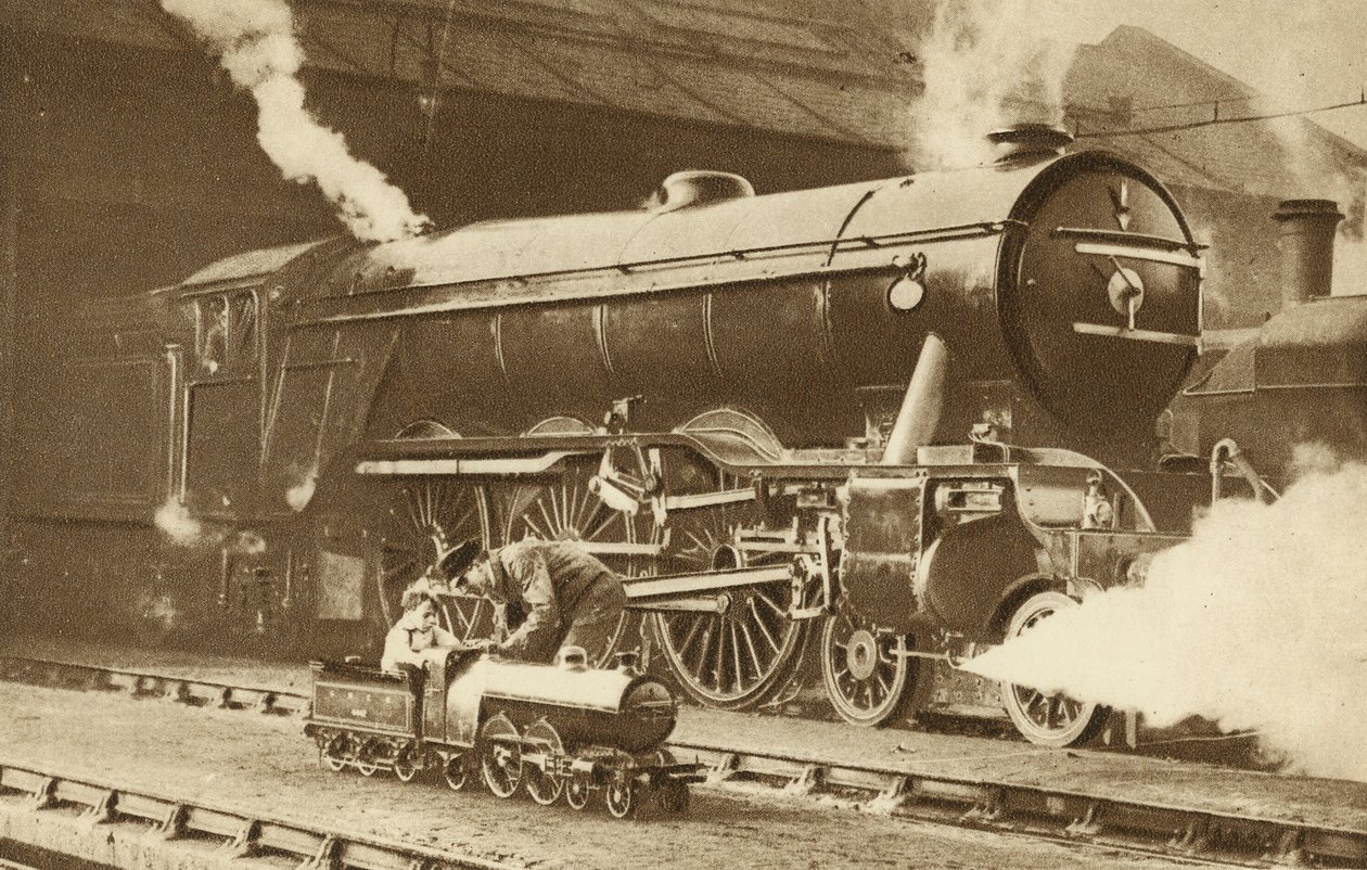 Jongen rijdt op een speelgoedstoomlocomotief voor de echte (z/w foto) door English Photographer