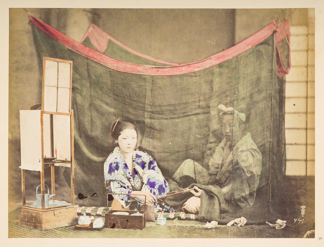 Japans stel in hun vrije tijd, Studiotableau van een jonge Japanse vrouw, zittend met theebenodigdheden om haar heen, die een pijp aanreikt aan een mannelijke figuur die achter haar zit, afgeschermd door een linnen muskietennet, Fotograaf: Onbekend Lucas C door English Photographer