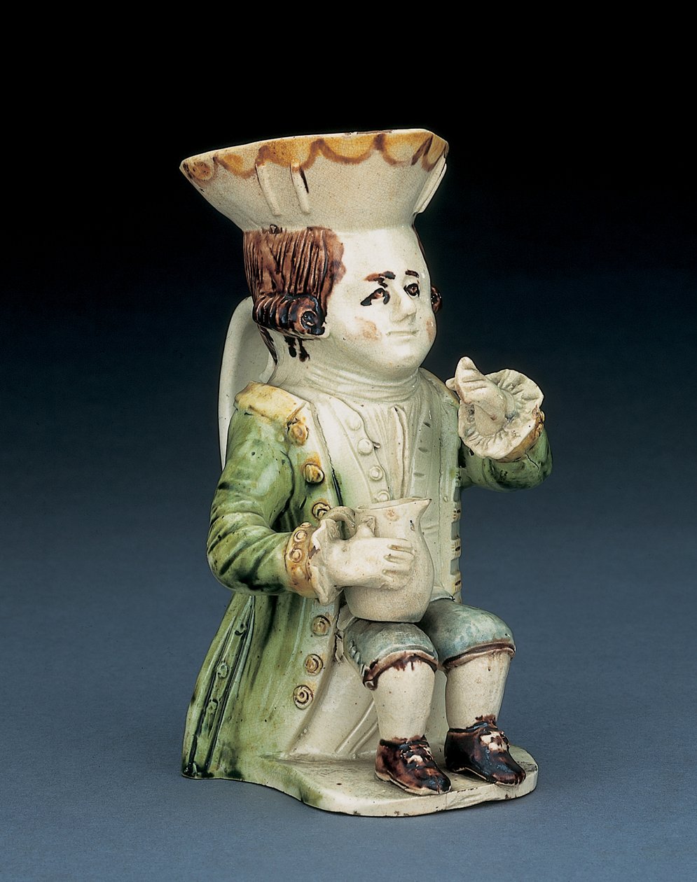 Toper toby jug, zijn hoed met bruine en gele geschulpte rand, zijn ingekerfde bruine haar vastgebonden met een witte rozet, zittend met een balusterkan op zijn knie, c.1770 door English School