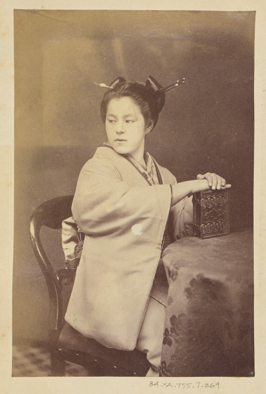 [Zittende Japanse vrouw die een cartes-de-visite album vasthoudt aan een tafel]. door Felice Beato