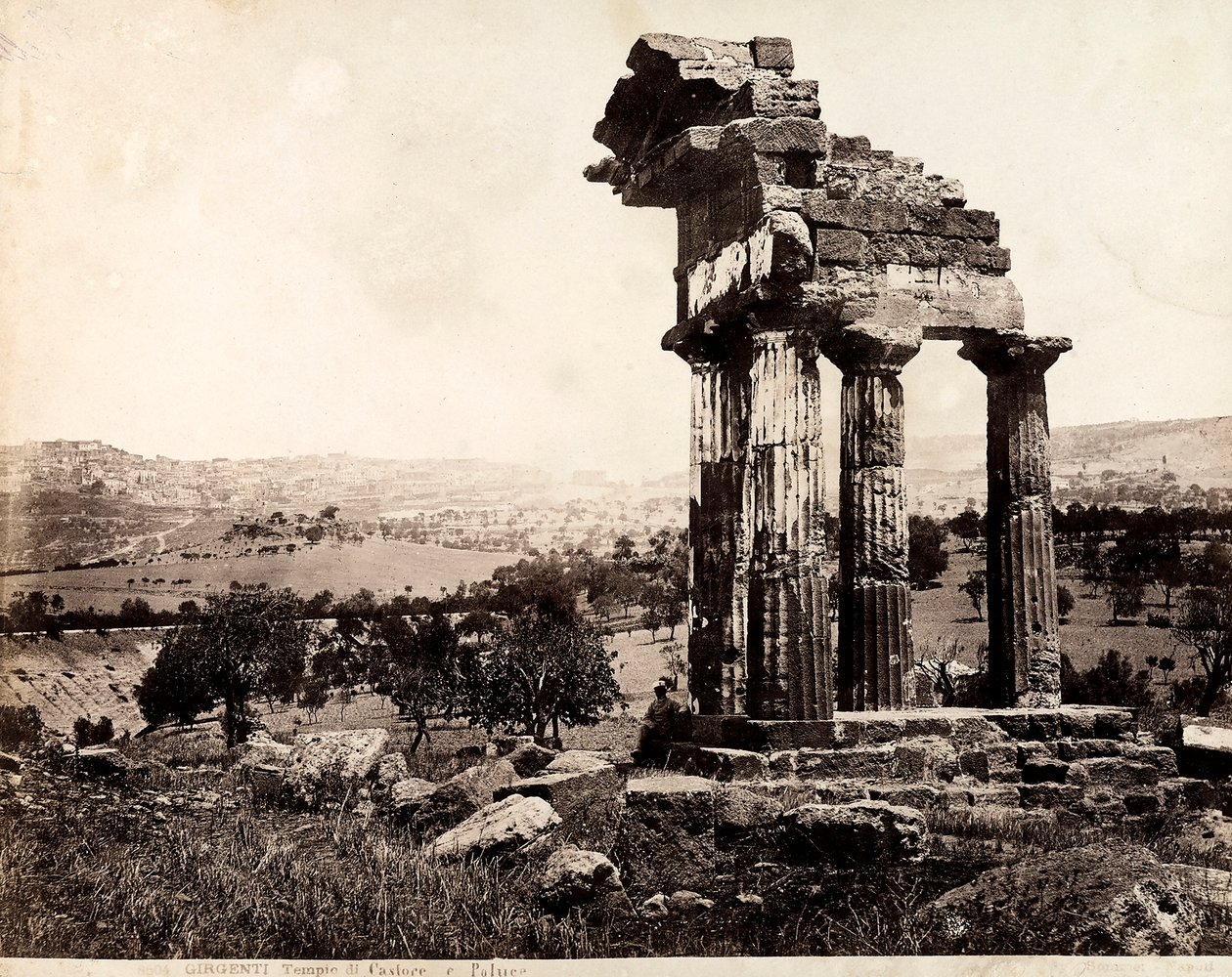 Uitzicht op de resterende vier kolommen die een hoofdgestel ondersteunen van de Tempel van Castor en Pollux in de Valle dei Templi, Agrigento. Een panorama van de stad is zichtbaar op de achtergrond door Giorgio Sommer