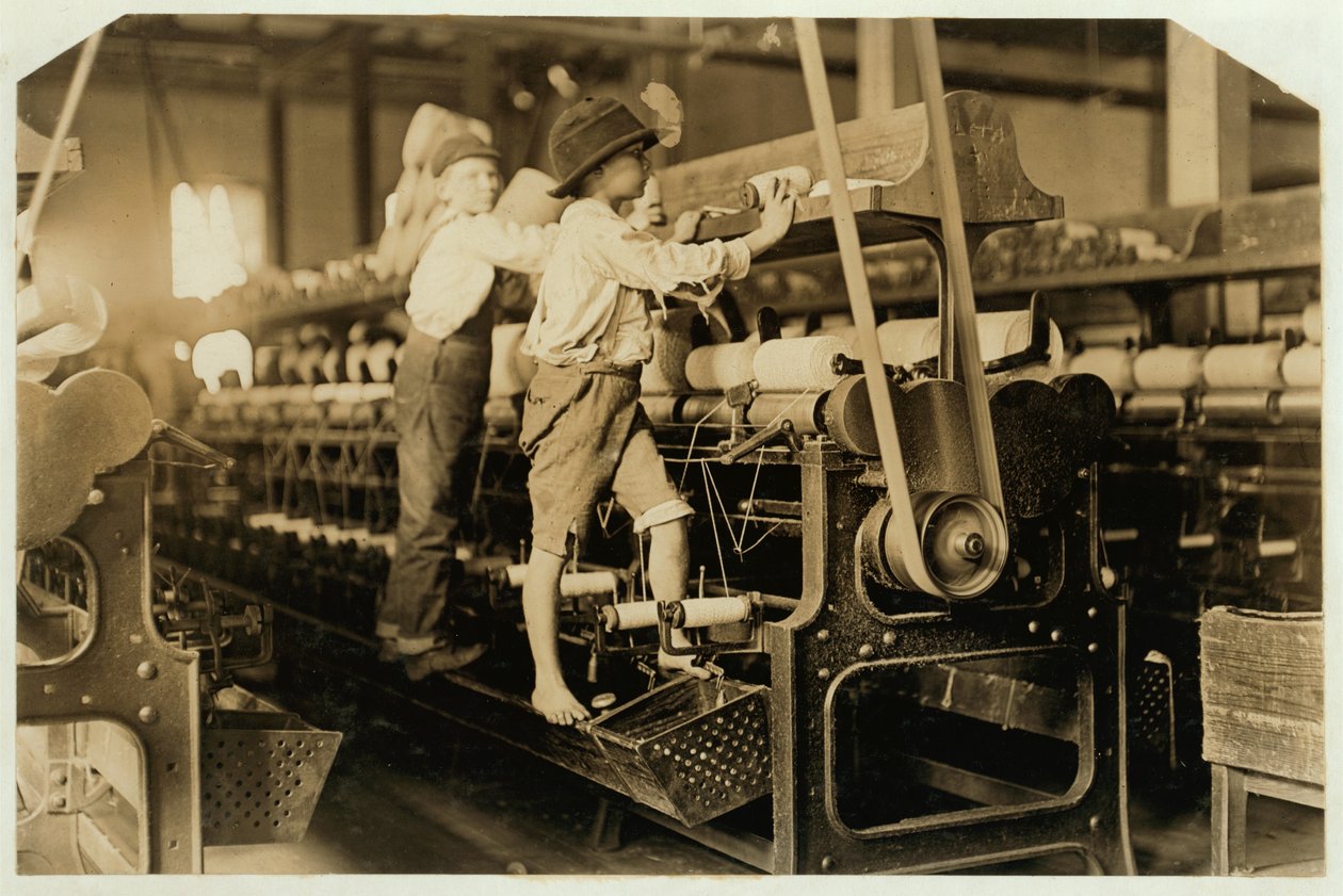 Kleine jongens klimmen op spinmachine om gebroken draden te repareren en lege spoelen te vervangen bij Bibb Mill, Macon, Georgia, 1909 door Lewis Wickes Hine