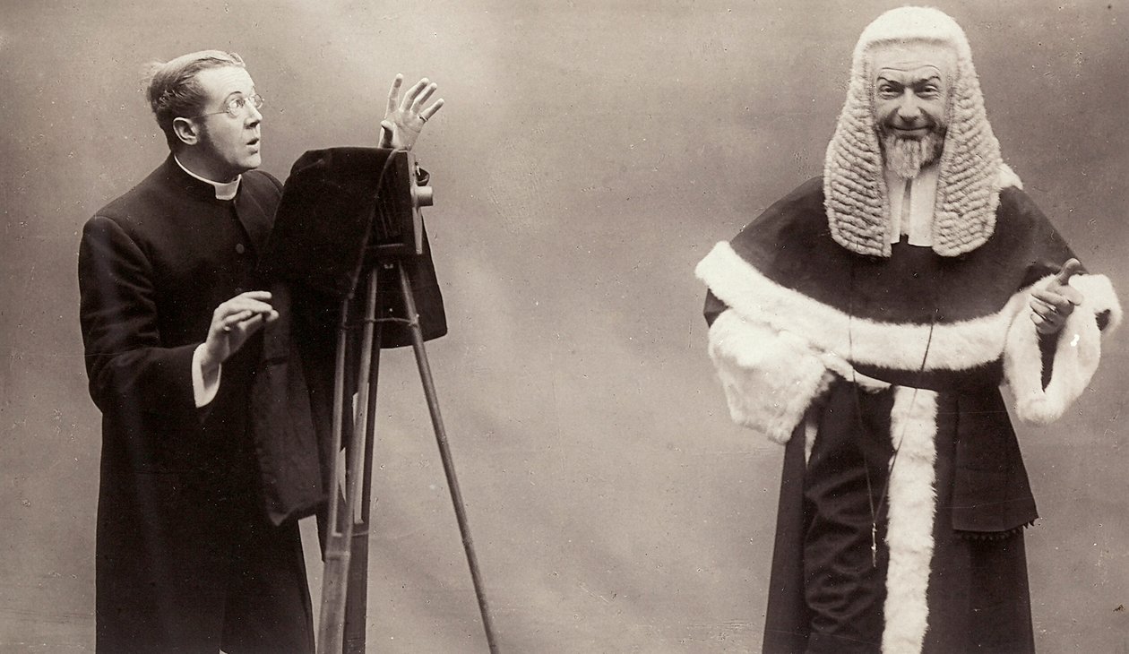 Een man in een soutane richt de lens van zijn camera op een man gekleed als een paus door Rotary Photographic Co Ltd