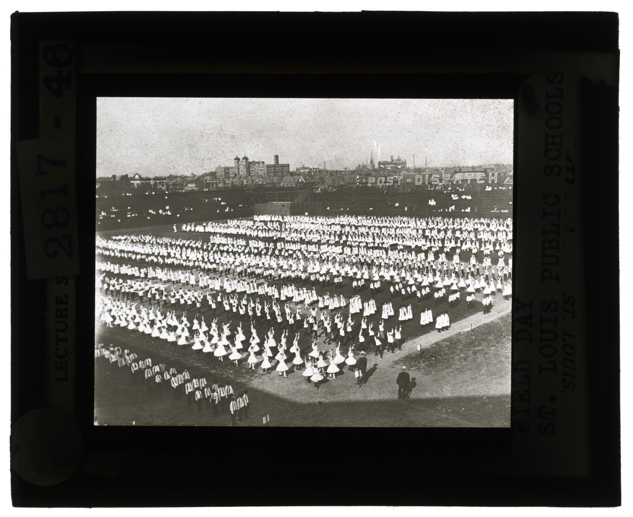 Horizontale, zwart-wit foto van honderden schoolkinderen in formatie voor Field Day parade en spektakel. Alle meisjes in witte jurken en de jongens in witte shirts en stropdassen met donkere broeken door Unbekannt Unbekannt
