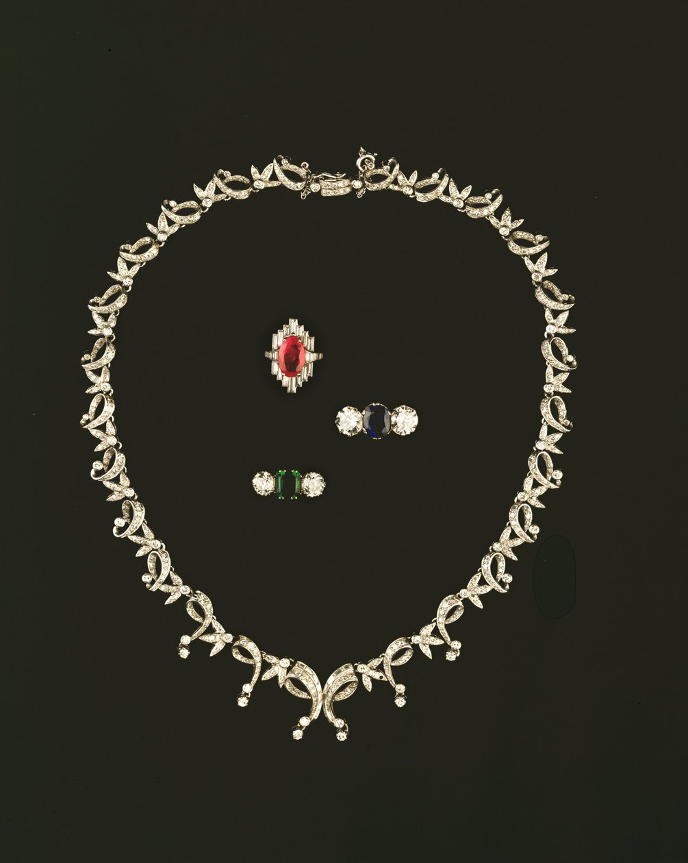 Art Deco ketting met rol- en bladontwerp; robijn- en diamantbaguettring; saffier- en diamantdriesteenring; smaragd- en diamantdriesteenring door Unbekannt Unbekannt