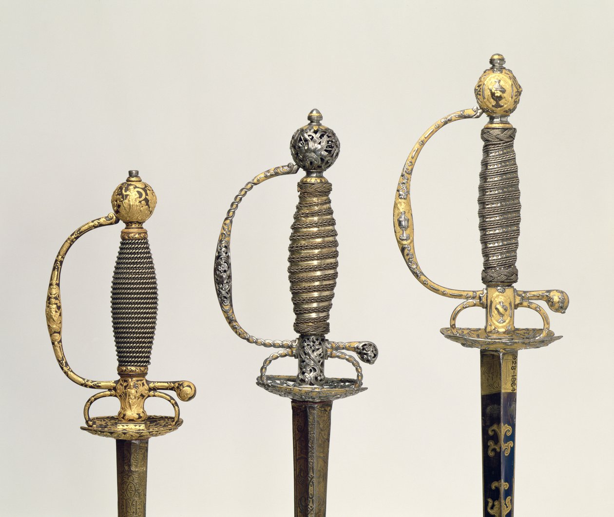 Heften van drie Franse zwaarden: een van staal, geblauwd en versierd met ontwerpen in gegraveerd goud, c.1730; een van staal, doorboord en gegraveerd en de grond van gematteerd goud, c.1760; een van gegraveerd staal door Unbekannt Unbekannt