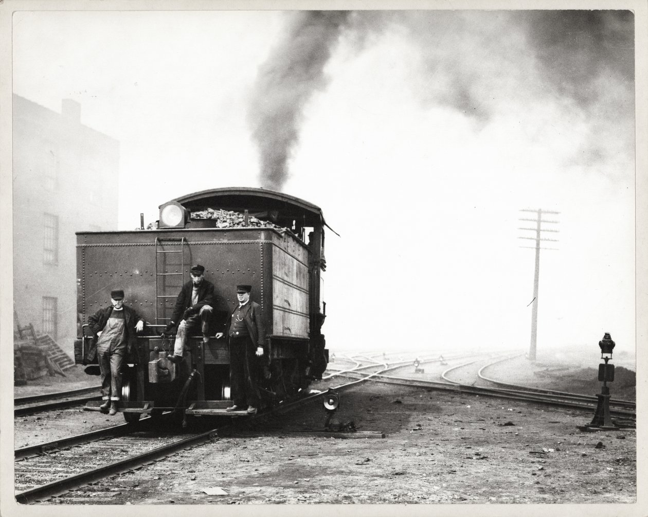 Drie mannen op de achterkant van een rangeerlocomotief in een onbekende spoorwegwerf door Unknown
