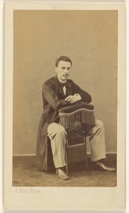 [Man met snor, zittend, met voorkant naar achterkant van stoel met franje]. door Alexandre Ken