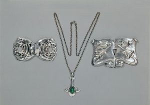 Zilveren sieraden ontworpen voor Liberty. Van links naar rechts: Taille gesp met verstrengeld Keltisch ontwerp, 1904. Hanger en ketting met cabochon geslepen chrysopraas. Taille gesp met repoussé ontwerp op gehamerd door Archibald Knox
