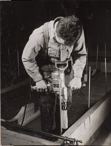 [Man gebruikt een handbediende machine om een stuk hout te bewerken].