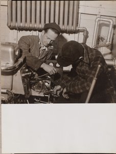 [Twee mannen werken aan een machine met een schroevendraaier en een moersleutel].