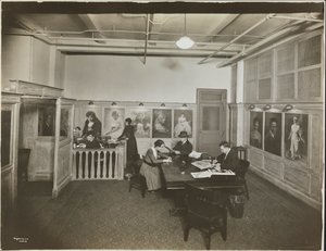 Hoofdkantoor/receptiekamer bij de Mutual Film Co. met secretaresse aan het bureau, mensen aan een tafel lezend, en portretten aan de muur, New York