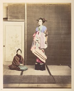 [?Geisha,] Volledig staand studiportret van een jonge vrouw op verhoogde schoenen, haar jonge bediende knielend op de vloer naast haar door English Photographer