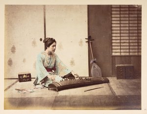 Zingende meisjes [Japan], Studiportret van een jonge Japanse vrouw zittend op een tatami-mat die een snaarinstrument bespeelt, Fotograaf: Onbekend Lucas Collectie: Fotografisch verslag van de wereldreis van Charles James en Morton P, Lucas