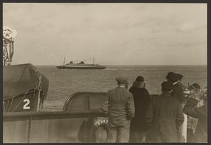 [Groep mensen op het dek van een schip die kijken naar een ander schip dat in de verte voorbij vaart].