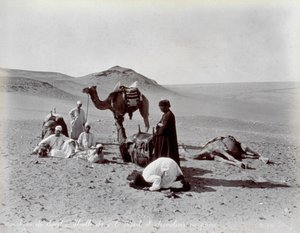 Egyptische kameeldrijvers tijdens een pauze in de woestijn. Op de voorgrond lijken twee leden van de kleine groep te bidden