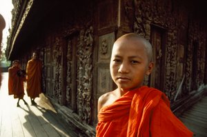 Een jonge novice monnik voor gebeeldhouwde teakpanelen. Shwenandaw-klooster, Mandalay, Birma