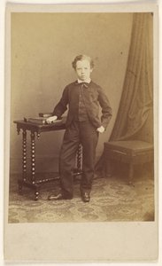 [Ongeïdentificeerd jongetje in pak staat bij een tafel met boeken erop]. door Joseph Brown