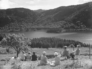 Groep mensen zittend op gras of ligstoelen kijkend naar uitzicht op Thirlmere door Joseph Hardman