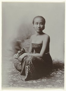 Studioportret van een zittende jonge Javaanse vrouw in een sarong met batik motief