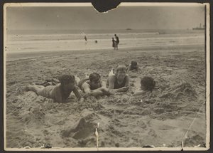 [Kinderen liggen in het zand op het strand].