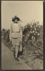 [Vrouw loopt langs hek met bloemen]. door Louis Fleckenstein