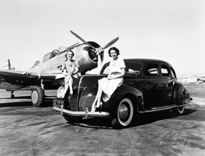 Californië: 1939 Twee Vrouwen Zitten op de Spatborden van een 1939 Lincoln Zephyr Sedan op een Vliegveld met een Eenmotorig Vliegtuig Geparkeerd Achter Hen (zw/w foto)