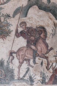 Detail van het mozaïek van de kleine jacht. Een jager staat op het punt een haas te spietsen. 3e - 4e eeuw. Romeinse Villa van de Casale, Sicilië. UNESCO-site.