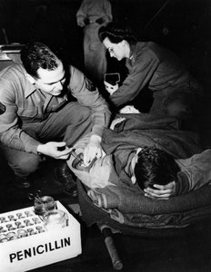 Tweede Wereldoorlog (1939-1945): Luxemburg februari 1945: In een evacuatieziekenhuis van het Amerikaanse leger dient een medicus (verpleegster) penicilline toe aan een gewonde soldaat om infectie te voorkomen terwijl een verpleegster hem voorbereidt op een door Unbekannt