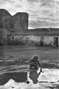 Jong meisje spelend met een papieren bootje in een plas omgeven door modder, Venosa, Basilicata, Italië door Unbekannt