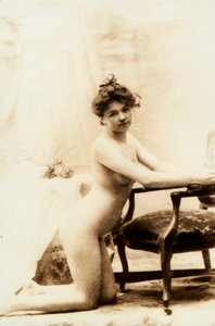 Naaktportret van een jonge vrouw knielend voor een kleine fauteuil
