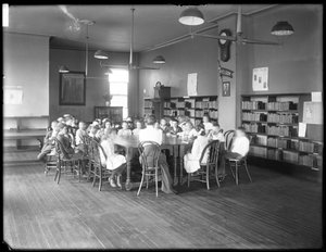 Kinderen luisteren naar een vrouw in de leeszaal van een niet-geïdentificeerde vestiging van de Queens Borough Public Library, ca. 1910 door William Davis Hassler