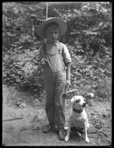 William Gray Hassler in strohoed en overall, met visstok en mand, geposeerd in het bos met een kleine hond (Bessie), 20 augustus 1911