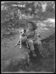 William Gray Hassler in strohoed en overall, zittend in het bos met een kleine hond (Bessie), 20 augustus 1911