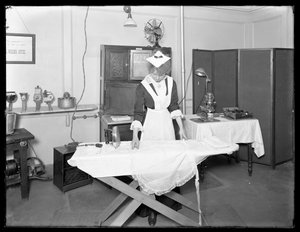 Jonge vrouw in een dienstmeisjeskostuum demonstreert het gebruik van een elektrische strijkijzer, ca. 1913-14 door William Davis Hassler