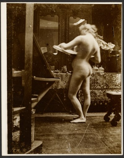 [vrouwelijk naaktmodel staand in studio met schetsboek]. door Alphonse Maria Mucha
