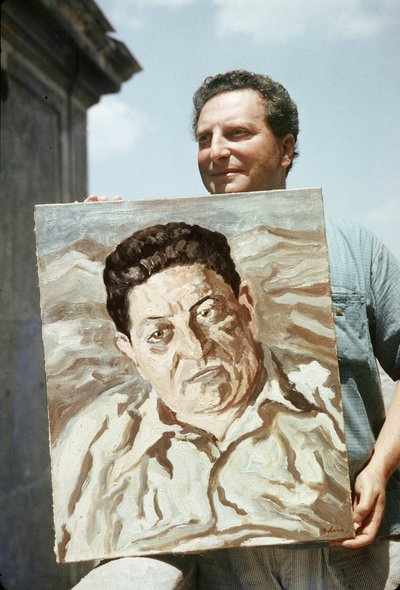 De Italiaanse schilder en schrijver Carlo Levi (1902-1975) met een van zijn werken in de hand, een portret van de vakbondsman Giuseppe di Vittorio (foto) door Ando Gilardi