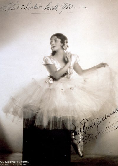 Portret van de klassieke ballerina Rosa Piovella Ansaldo, in tutu en balletschoenen. Ze zit frontaal, haar gezicht naar één kant gedraaid. Stoffen rozen versieren haar kleding en zorgvuldig gekapte haar (Milaan, Teatro alla Scala) door Baccarini and Porta