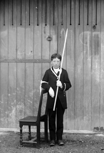 Eerste communicant, in wit kostuum en handschoenen, met medailles, rozenkrans, witte kanten manchet en een zeer lange kaars, nabij Bourmont in Haute-Marne, circa 1880. Fotografie. Ducos Collectie door French Photographer