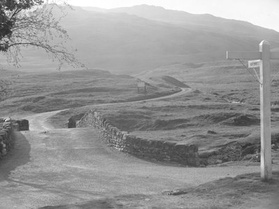 Zicht op de weg over de Hardknott Pass met een bord dat in de richting van Hardknott wijst door Joseph Hardman